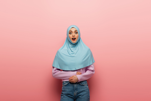 mujer árabe asombrada en hijab y jeans mirando a la cámara sobre fondo rosa - Foto, imagen