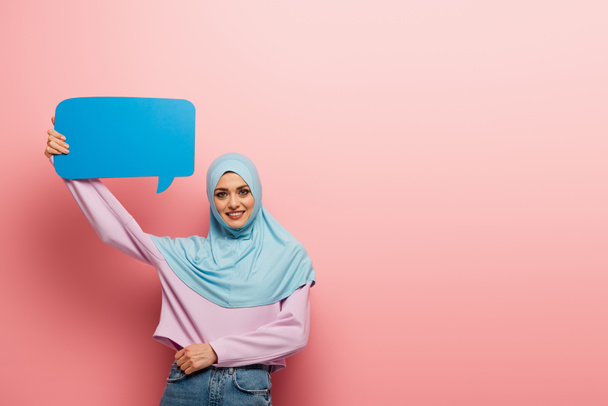 joyful arabian woman in blue hijab holding speech bubble on pink background - Photo, Image