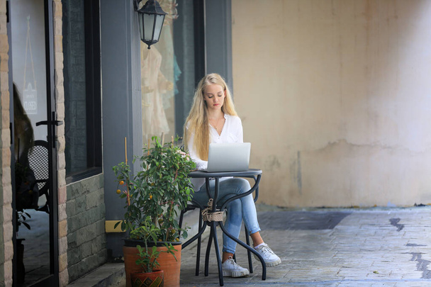 Güzel sarışın kız dizüstü bilgisayarla perakende mağazasının önünde oturuyor, küçük işletme sahibi kavramı. - Fotoğraf, Görsel