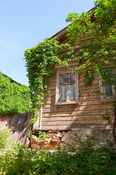 oude houten huis met groene planten over blauwe hemel - Foto, afbeelding
