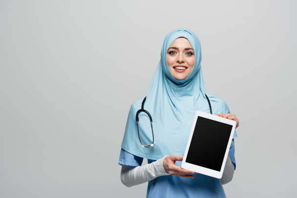 médecin musulman souriant tenant tablette numérique avec écran blanc isolé sur gris - Photo, image