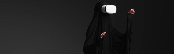muzułmańska zakonnica gestykuluje podczas gry w vr słuchawki izolowane na czarnym, baner - Zdjęcie, obraz