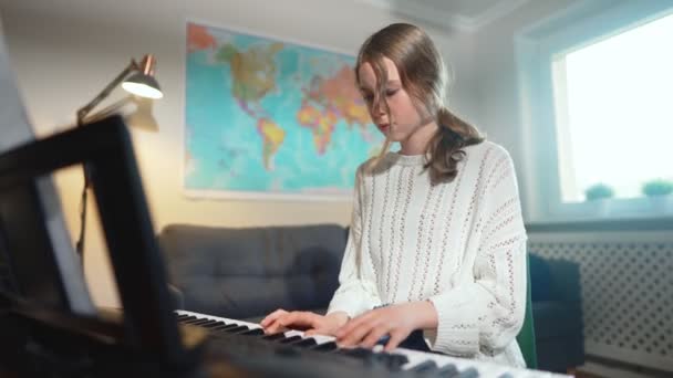 Девочка-подросток играет на электронном музыкальном инструменте дома. - Кадры, видео