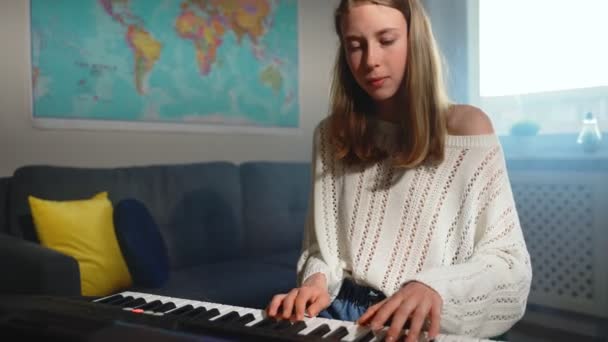 Девочка-подросток играет на электронном музыкальном инструменте дома. - Кадры, видео