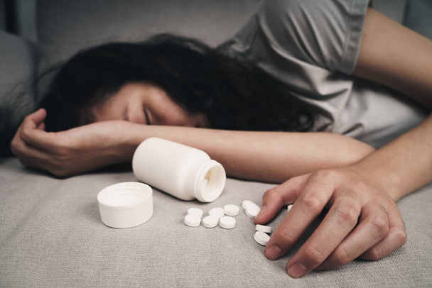 Donna che prende overdose di medicina e sdraiata sul divano con flacone di pillole aperto. overdose e suicidio Concetto. - Foto, immagini