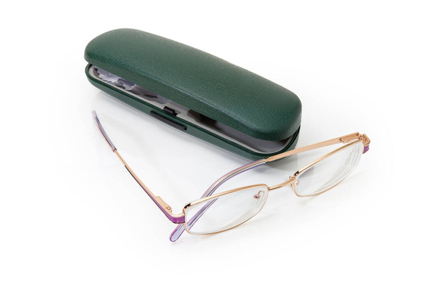Metal sarısı çerçeveli kadınlar için modern klasik gözlükler. Mor elementler beyaz bir yüzey üzerinde yeşil sert gözlük kılıfına karşı. - Fotoğraf, Görsel