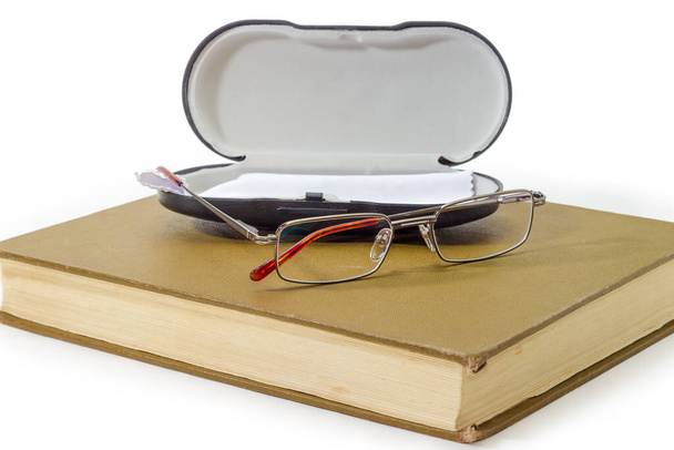 Moderní klasické brýle pro muže v kovovém ráfku proti tvrdé vitríně na uzavřené staré velké knize na bílém povrchu, detailní záběr ve výběrovém ohnisku - Fotografie, Obrázek
