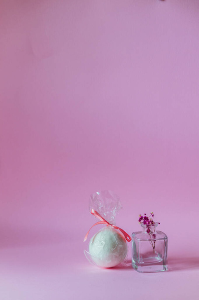 Bombe de bain blanche à côté d'un petit vase sur fond rose avec espace vide. - Photo, image