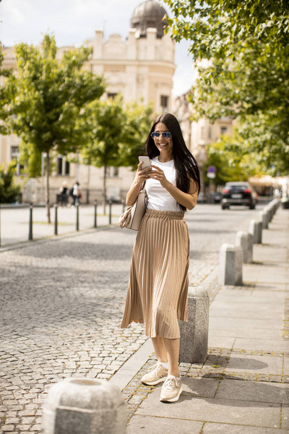 Красива молода жінка використовує мобільний телефон під час ходьби на вулиці
 - Фото, зображення