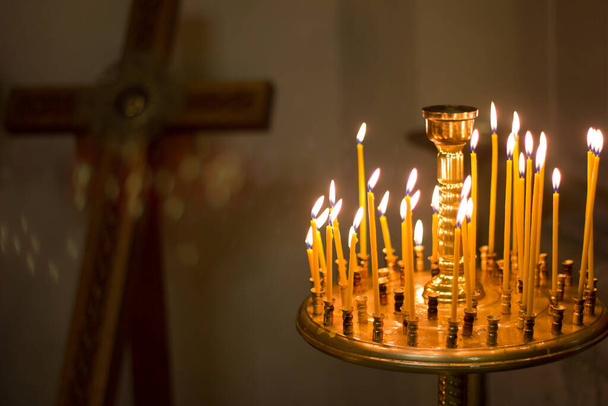 Свічки, що палять у церкві на тлі хреста, молитви за здоров'я і мир душі, церковного інтер'єру, християнського свята. - Фото, зображення