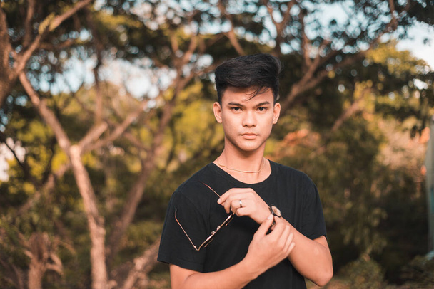 A strikingly handsome young Filipino man at the park. In a black t-shirt. At the park during late afternoon. - Photo, Image