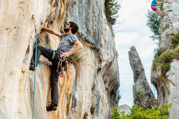 Człowiek z liną, łukiem i haczykami wspinający się na pionową ścianę skalną w górach. sporty górskie i przygoda - Zdjęcie, obraz