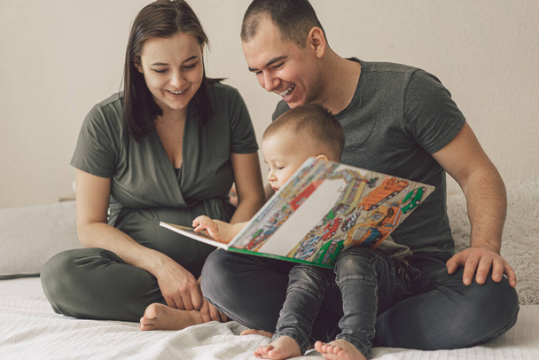Amor familiar. Padres e hijo pequeño leyendo libro juntos en casa en el dormitorio. La vida familiar es sobre diversión. - Foto, Imagen
