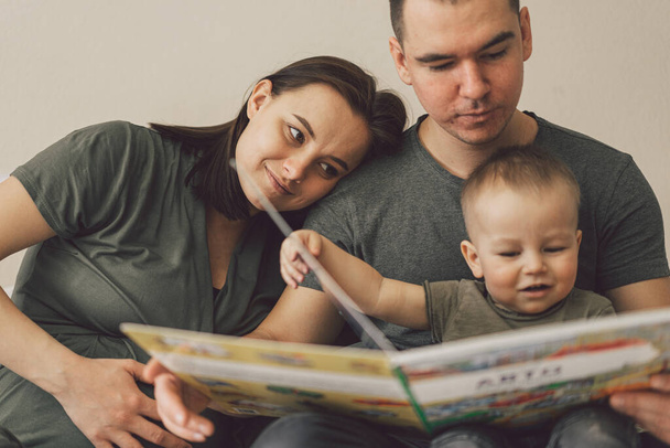 Familienliebe. Eltern und kleiner Sohn lesen gemeinsam Buch zu Hause im Schlafzimmer. Im Familienleben geht es um Spaß. - Foto, Bild