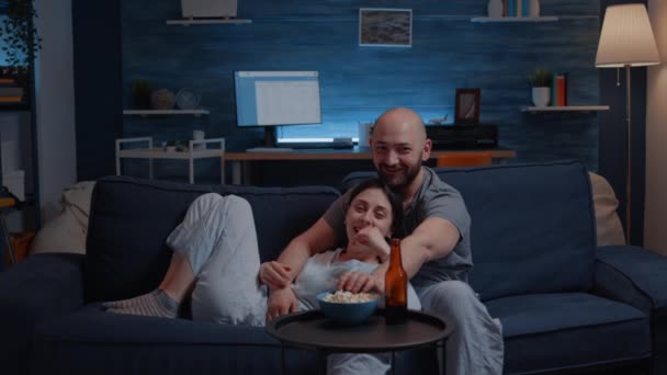 Hermosa pareja feliz viendo la televisión en el sofá relajándose por la noche riendo - Metraje, vídeo