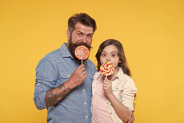 Happy family dad and daughter eat lollipop yellow background, homemade caramel concept - Фото, зображення