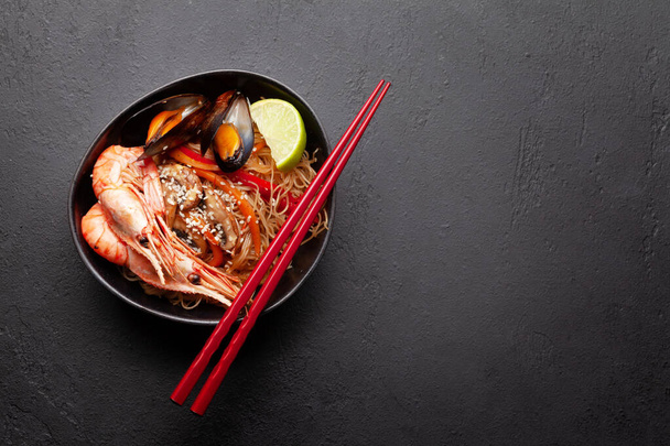 Wok with stir fried noodles, shrimps and vegetables on stone background. Top view flat lay with copy space - Photo, Image