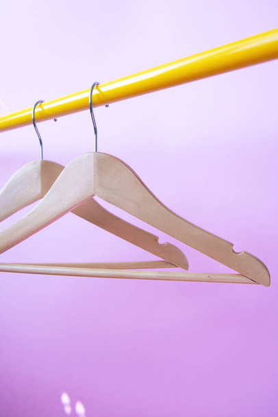 Two wooden clothes hangers hang on a yellow rack on a violet background - Foto, Imagem