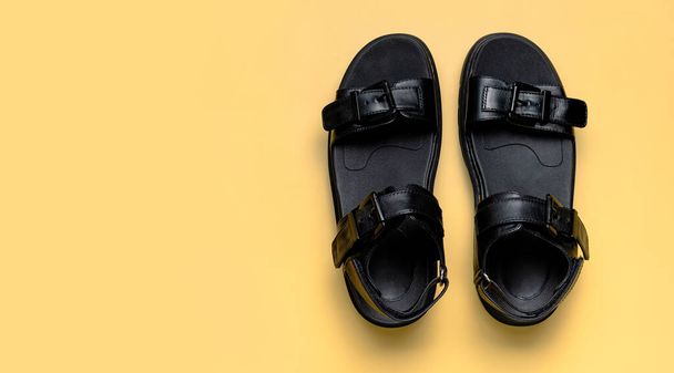 Sandales d'été en cuir noir pour femmes sur fond sablonneux beige plat lay top view copy space. Chaussures féminines à la mode, sandales rugueuses à semelles épaisses. Concept minimaliste, publicité pour les pieds. - Photo, image