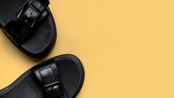 Черные кожаные летние женские сандалии на бежевом песчаном фоне плоски лежат сверху. Модные модные женские туфли, грубые сандалии с толстыми подошвами. Минималистическая концепция, реклама ног. - Фото, изображение