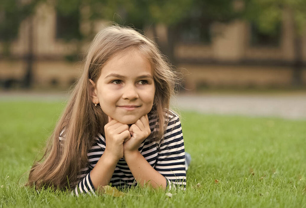 Happy little kid smile mit gesunder Gesichtshaut und langen Haaren liegt auf grünem Gras natürliche Sommerlandschaft, Hautpflege - Foto, Bild