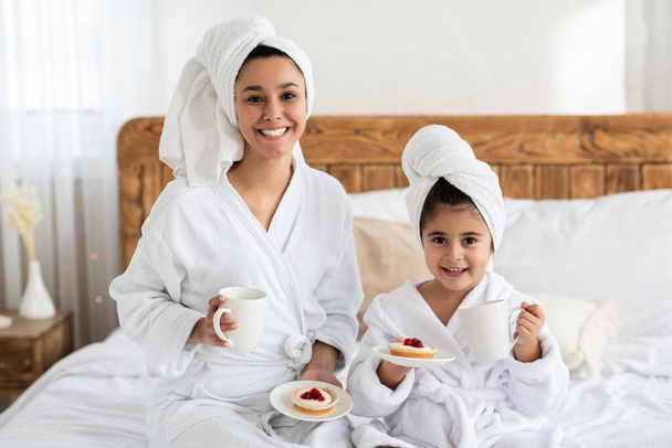 Onnellinen äiti ja tytär kylpytakit juominen teetä kakkuja - Valokuva, kuva