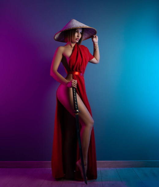 sexy woman in a red cape and an Asian hat with a katana in her hand image of a samurai in neon color - Fotoğraf, Görsel