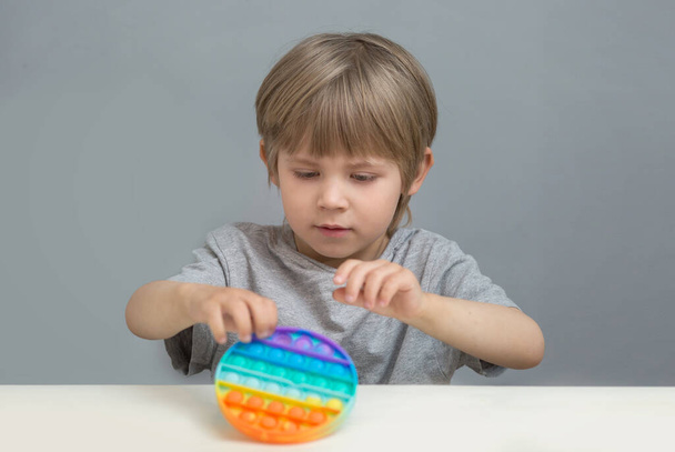 the child is holding a silicone antistress pop it toy with a round shape and rainbow color - Zdjęcie, obraz