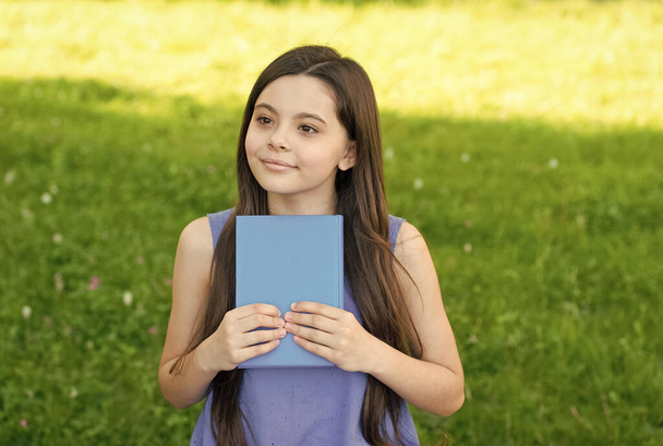 Book a day keeps boredom away. Small girl hold book outdoors. Little reader on summer day. Library book. Fantasy and fiction. Literature and poetry. Reading habit. Get lost in good book - Foto, imagen