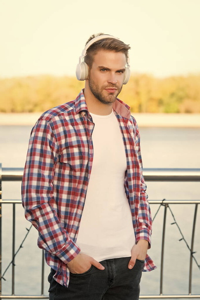 young handsome man in checkered shirt wear modern headphones listening music outdoor, music - Фото, изображение