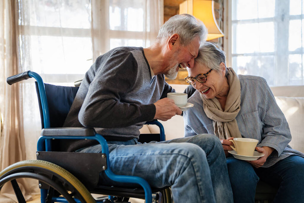 Romantic happy senior couple in love at home. Mature man with disability in wheelchair having fun with wife - Fotoğraf, Görsel