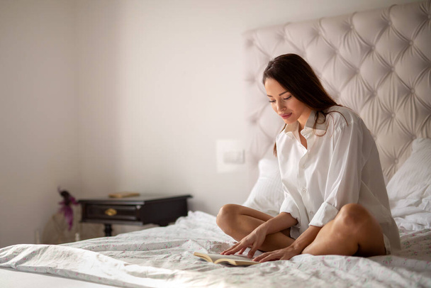 Beautiful young woman relaxing reading book on weekend at home - 写真・画像