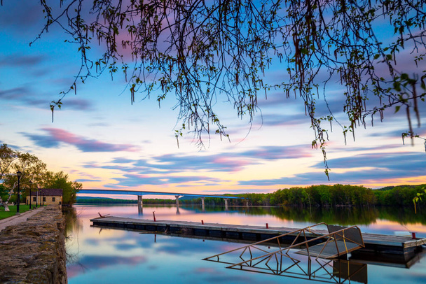 Vue du paysage du pont traversant le fleuve Mississippi par une longue exposition et une longue vitesse d'obturation pendant les heures bleues lever ou coucher du soleil avec une ancienne passerelle de pont ponton au premier plan. - Photo, image