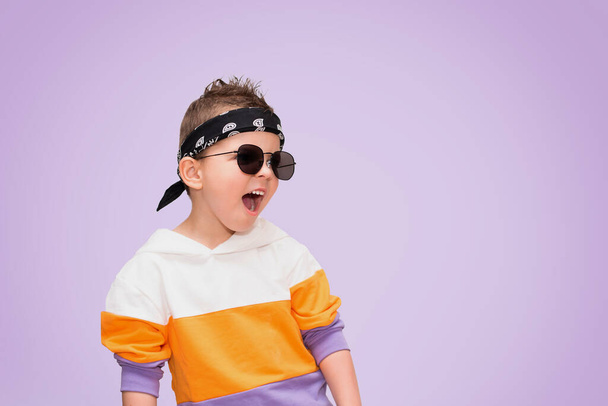 Μικρό δροσερό αγόρι με κομψά ρούχα και γυαλιά ηλίου κραυγές. - Φωτογραφία, εικόνα