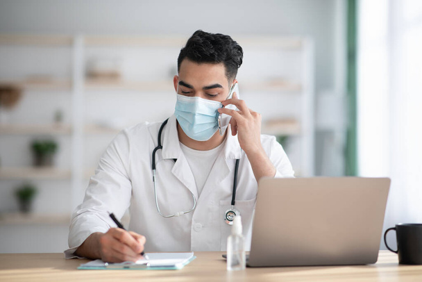 Dokter in het gezicht masker werken in de kliniek, met een telefoontje - Foto, afbeelding