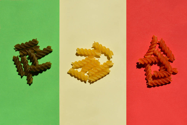 Close up of dry uncooked fusilli tricolore on green, pale yellow and red paper - Foto, Bild