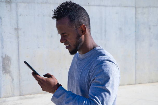 afro-amerikai férfi nézi a mobiltelefonját, mert kapott információt SMS-ben vagy e-mailben - Fotó, kép