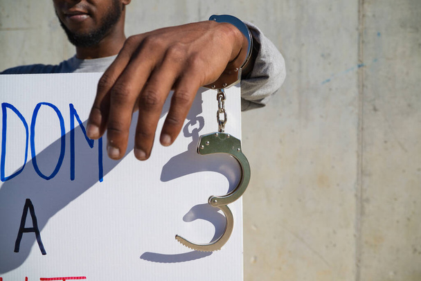 El hombre afroamericano sostiene una pancarta que dice que la libertad es un derecho. El hombre sostiene un grillete o esposas en su mano izquierda. Derechos humanos. Detener el racismo. Las vidas negras importan. - Foto, imagen