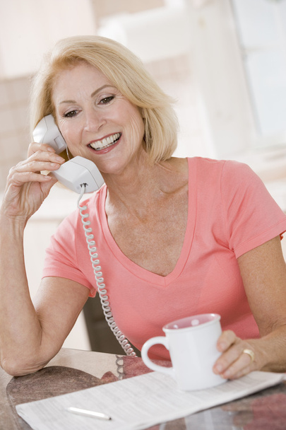 Woman in kitchen with coffee using telephone smiling - Valokuva, kuva