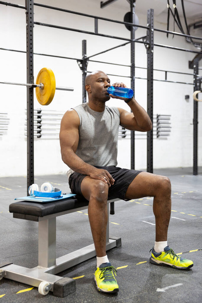Black male athlete drinking water after workout in gym. Sport and healthy lifestyle. - Photo, Image