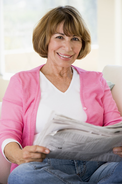 Woman relaxing with newspaper in living room and smiling - Фото, изображение