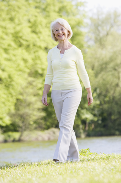 Woman walking outdoors at park by lake smiling - Foto, afbeelding
