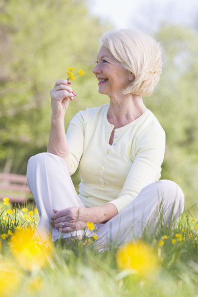 Woman sitting outdoors smiling and holding a Buttercup flower - Valokuva, kuva