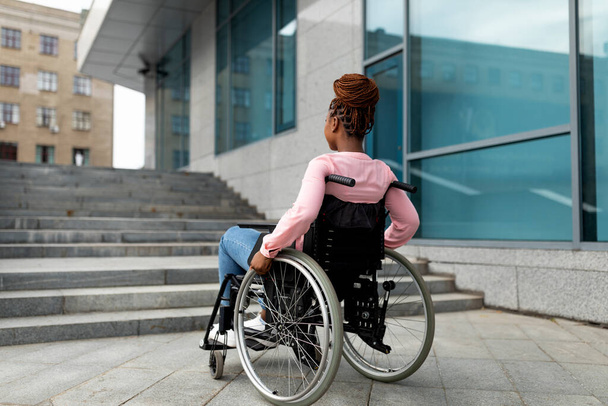 Young black impaired lady in wheelchair cannot go up stairs without ramp, feeling limited and unhappy, copy space - Photo, Image