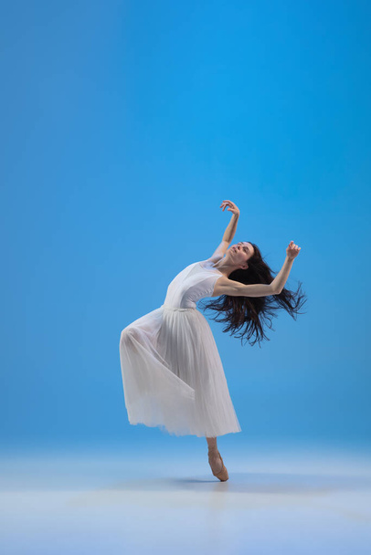 Young and incredibly beautiful ballerina is posing and dancing at blue studio full of light. - Foto, Bild