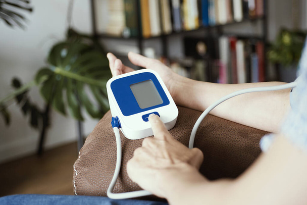 closeup of a caucasian man, sitting on the brown couch of his living room, measuring his blood pressure with an electronic sphygmomanometer - Foto, afbeelding