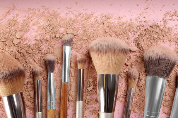 Makeup brushes and scattered face powder on pink background, flat  lay - Foto, imagen