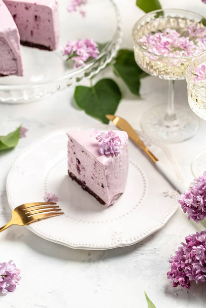 a piece of mousse cake, Delicious dessert blueberry tart with fresh berries with a bouquet of purple blooming lilacs, vertical image place for text, - Valokuva, kuva
