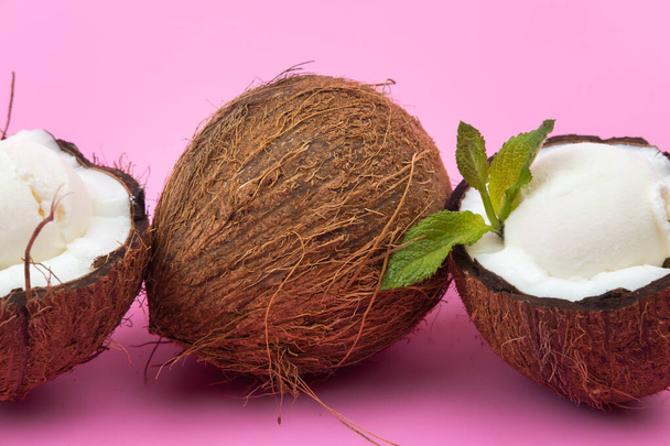 Vanilla ice cream balls in fresh coconut halves decorated with mint leaves on a pink background. - Foto, Imagem