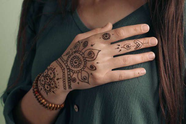 Woman with beautiful henna tattoo on hand against green background, closeup. Traditional mehndi - Φωτογραφία, εικόνα